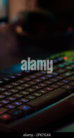 Close up of professional keyboard with RGB lighting prepared for streaming online tournament, display with first person shooter playing on it. Gaming studio of esport video game with powerful computer Stock Photo