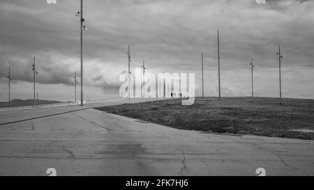 Urban landscape on a overcast day. Four boys walking in the distance along a footpath in the large esplanade of Barcelona's Forum Park. Stock Photo