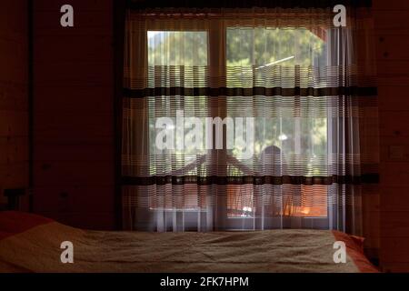 Relaxation and rest. Window by the bed in the guest room of the wooden cottage. Stock Photo
