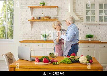 Loving senior couple having fun and dancing waltz while cooking healthy meal together Stock Photo