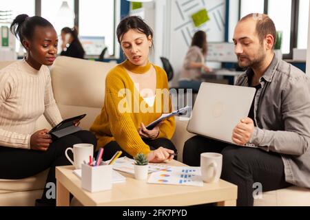 Friendly creative diverse colleagues team discussing about business project using laptop and tablet at workplace. Multiracial coworkers group working together sharing marketing ideas at office meeting Stock Photo