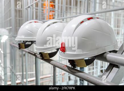 White safety helmets hanging on wall at the factory. Construction engineer safety white headgear Stock Photo