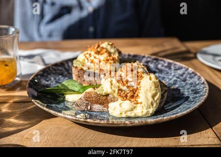 Two pieces of toasted whole rye bread with mashed avocado, poached eggs and sauce. Sandwiches with egg, avocado and sauce. Selective focus. Stock Photo