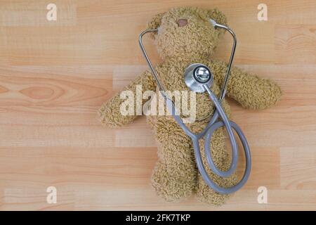 Teddy bear on wooden floor with stethoscope, acoustic medical device with earpieces in ears Stock Photo