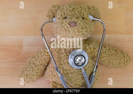 Teddy bear on wooden floor with stethoscope, acoustic medical device with earpieces in ears Stock Photo