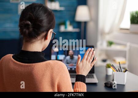 Student greeting her school teacher during online videocall meeting. Young woman talking about math lesson on university webinar while sitting at desk table in living room Stock Photo