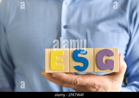 Man holds wooden ESG cube block, concept of checking company for business environmental friendliness for reliable investment. Environmental. Social. G Stock Photo