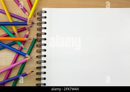 Top view of coloring colored pencils next to sketch drawing book on wooden background Stock Photo