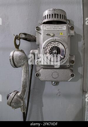 Old metal wall-mounted telephone with rotary dial. Text translation: When calling the dispatcher, push the lever down. Antique phone with dial Stock Photo