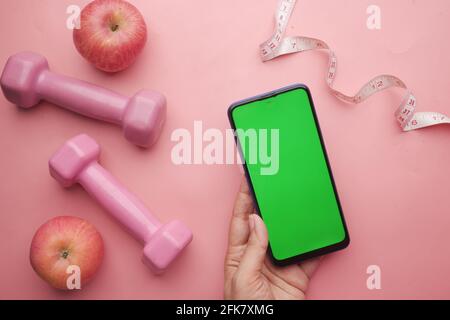 women hand holding Smart phone with s dumbbell and apple on pink  Stock Photo