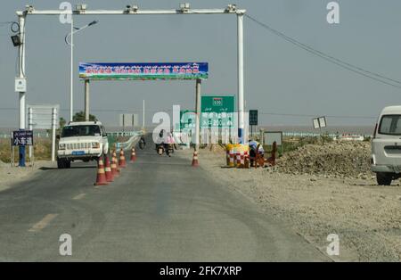 A policeman looks at his phone at a barriers on a road security checkpoint with cameras and face recognition to control the movement of Uighur (Uyghur) people on the outskirts of Kashgar in the South of  Xinjiang, China, PRC. © Time-Snaps Stock Photo