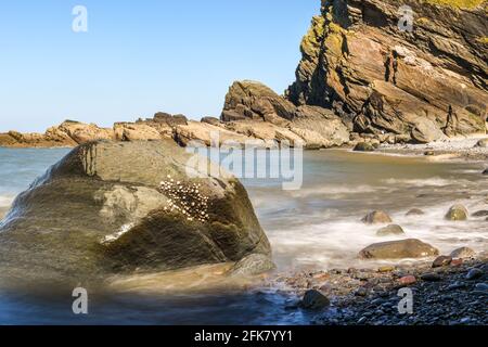Looking out over a calm blue ocean view of shoreline with sea waves crashing on rocks Stock Photo