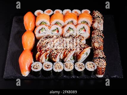 Japanese sushi set. Different types of appetizing rolls on a stone plate on a black background. Top view, flat lay. Stock Photo