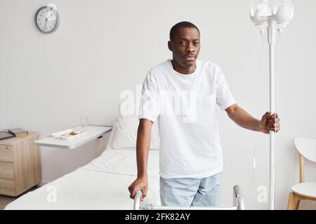 Waist up portrait of African-American man in hospital holding onto iv drip stand and looking at camera, copy space Stock Photo