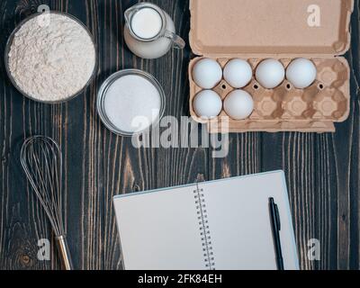 blank recipe book and flour, eegs, milk, sugar on wooden background. Stock Photo