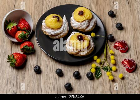 Composition of dish with typical Italian dessert called zeppole, strawberries, blueberries, heart-shaped chocolates and mimosa flowers Stock Photo