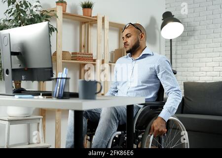Disabled african american man sitting at the table and working on computer Stock Photo