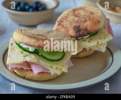 Breakfast with delicious toasted sandwiches topped with ham, cheese and cucumbers served on a rustic stoneware plate with a bowl of fresh berries Stock Photo