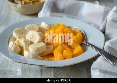 A plate with chopped bananas and oranges served on a white wooden table at home. Closeup view Stock Photo