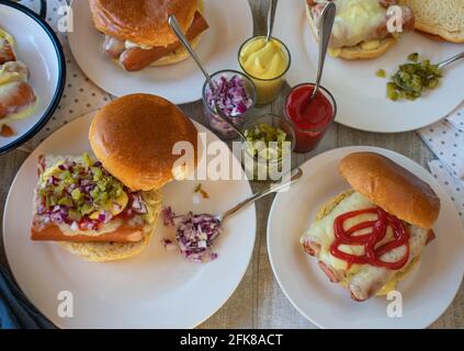 Dinner table with homemade fast food meal with hot dog burger with cheese, pickles, onions, mustard ketchup Stock Photo