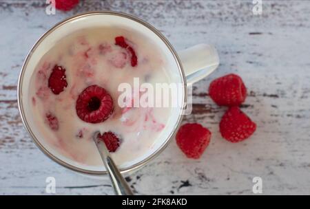 overhead view of a homemade fresh made raspberry yogurt in a white enamel cup on white weathered wooden background with copy space Stock Photo