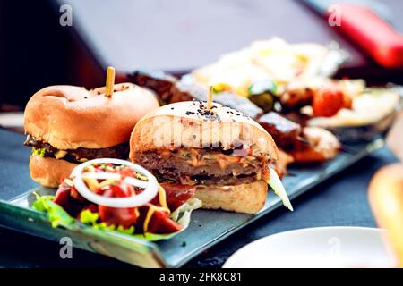 Two mini burgers with vegetables and herbs on a flat rectangular plate Stock Photo