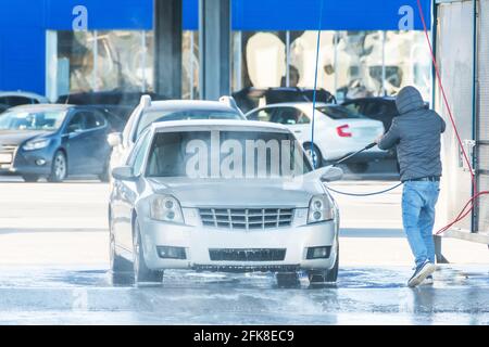 Man washing his car with using a high compression pressure water jet. Washing his car in a self-service car wash station Stock Photo