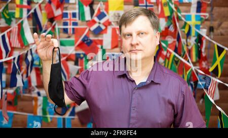 A man shares a used medical mask in his hands against the background of country flags. Stock Photo