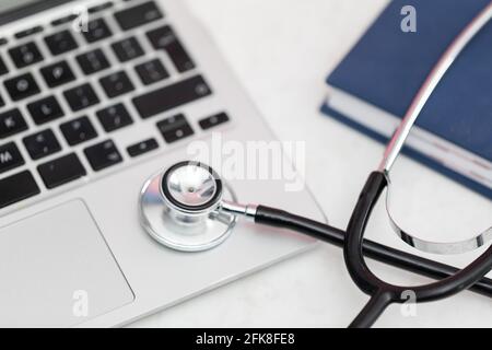 The stethoscope sits on the desk and next to it is a laptop and a book calendar. Stock Photo