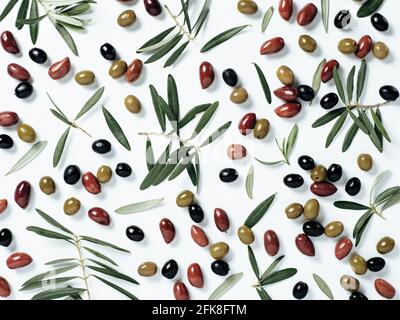 Beautiful pattern with green, black and red olives and olives tree leaves and branches on white background. Mix olive tree fruits and branches as pattern, top view or flat lay. Stock Photo