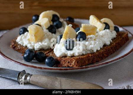 Healthy open faced sandwich with low fat cottage cheese, chopped bananas and blueberries served on a rustic plate for breakfast Stock Photo