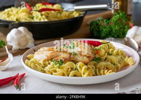 Healthy italian dish with pasta aglio e olio and fried fish served on plate on rustic kitchen table background Stock Photo