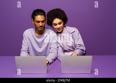 cheerful african american freelancers using laptops isolated on purple Stock Photo