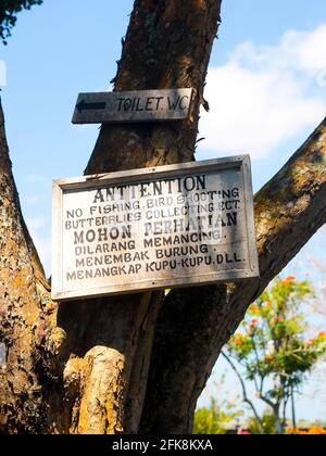 A handpainted white sign, prohibiting fishing, bird shooting, butterfly collecting. At the Tirta Gangga Water Palace in Bali, Indonesia. Stock Photo