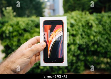 iPhone SE Special Edition 2nd generation in product red color - package against green park - hero object Stock Photo