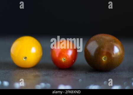 Close up of three colorful little tomatoes on dark background; colorful vegetable Stock Photo