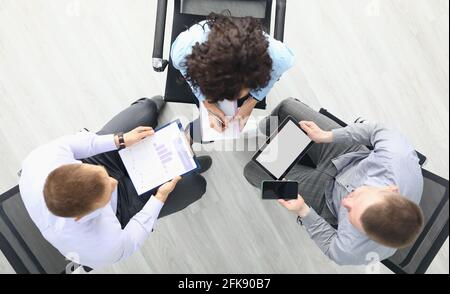 Business people sit on chairs with tablet and commercial business charts and discuss work plans top view Stock Photo