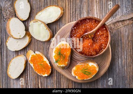 Red caviar in a bowl and sandwiches on old wooden background. Top view Stock Photo