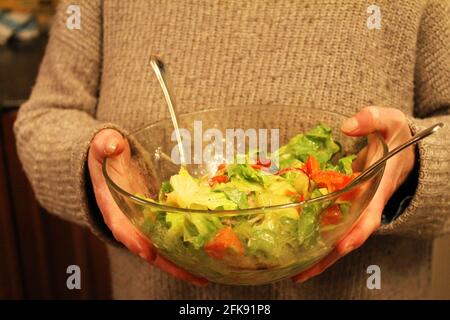 Close-up of a woman carrying a clear glass bowl with a fresh garden salad. Stock Photo