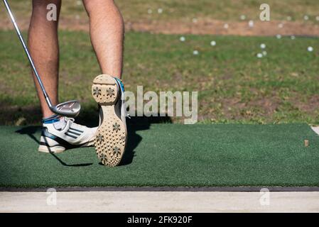 Close up of a young man hitting a golf ball at a driving range with the underside of his golf shoe visible Stock Photo