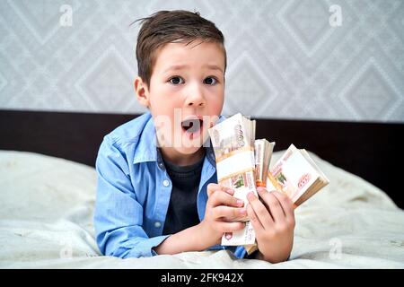 a little boy holds five-thousand-dollar bills in his hands and is happy. Stock Photo