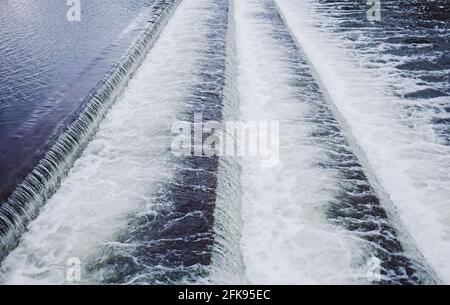 Foaming water coming over a small waterfall from a dam Stock Photo