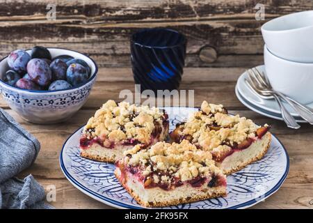 Three pieces of plum cake with crumble on a bluewhite plate on a wooden table Stock Photo