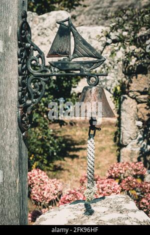 Rusty vintage metal bell with metal ship on the bracket, hanging on a wooden beam over a garden door Stock Photo