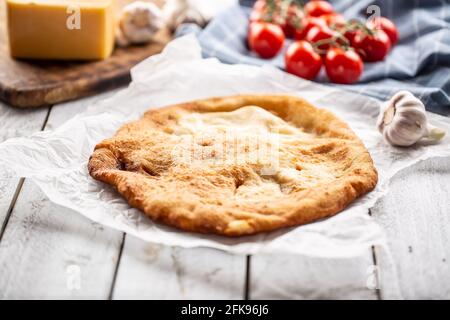 Traditional hungarian dish langos served on a baking paper in the background with garlic tomatoes and cheese on a wooden plate. Stock Photo