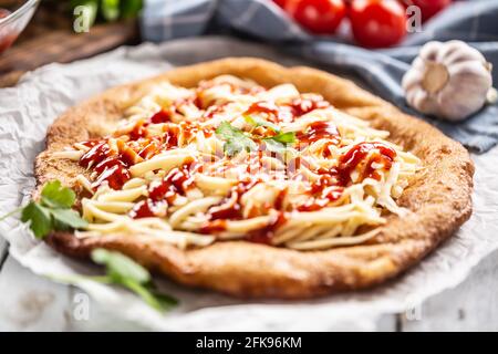 Deep-fried tastyful hungarian cheesy langos with poured ketchup, herbs and garlic. Stock Photo