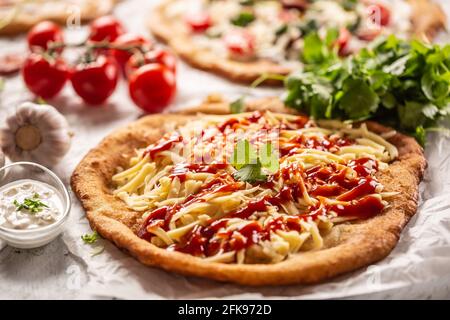 Cheesy hungarian traditionaly baked langos with ketchup, garlic and herbs served on a baking paper with tomatoes and vegetables and sour cream. Stock Photo