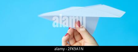 Female hand holding paper plane on blue background Stock Photo