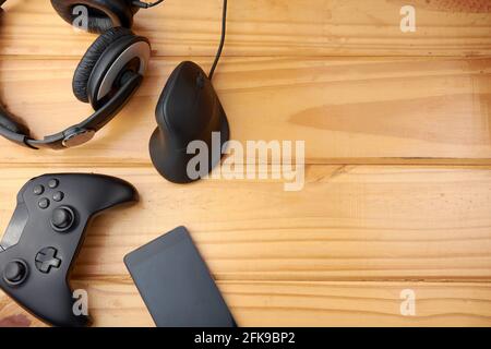Top view of ergonomic gaming accessories with game controller, vertical mouse, headphones and mobile phone on rustic wooden table. Stock Photo