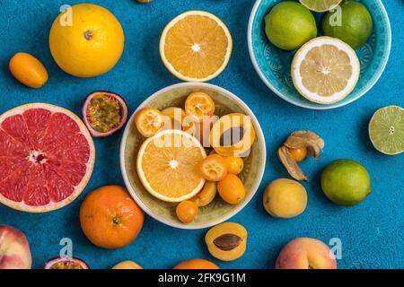 c Variety of tropical colorful summer fruits in bowls and on blue background, some of the citrus fruits sliced into halfs Stock Photo